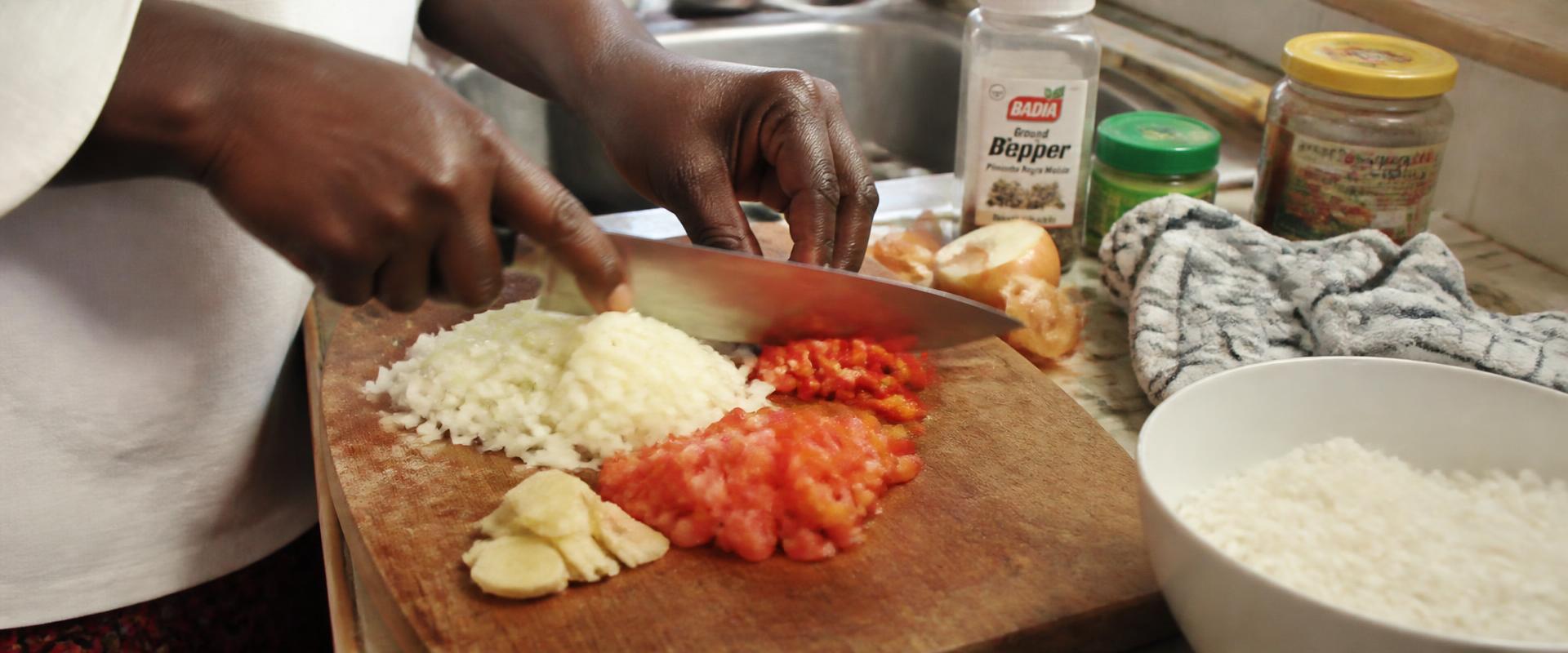 Hands chopping fresh peppers and onions on a wooden board in a sunlit kitchen